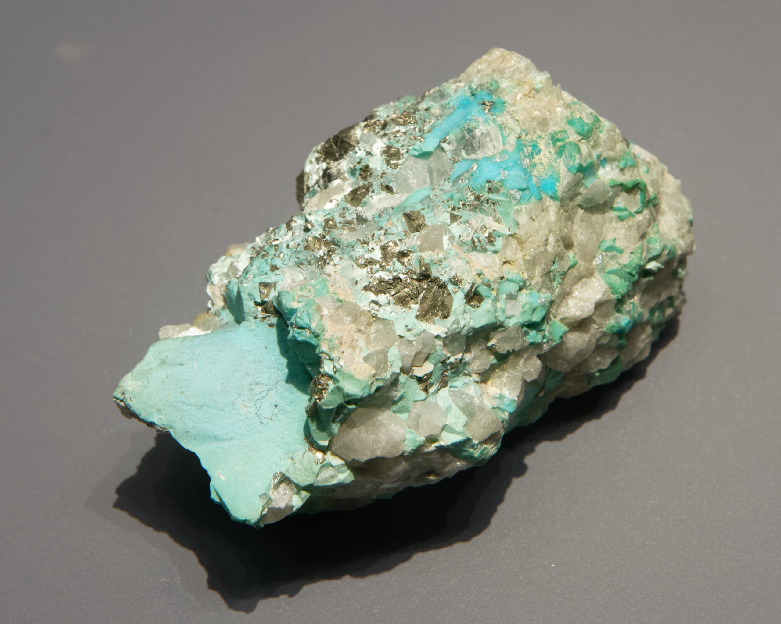 Blue-green turquoise within a pale rock matrix, photographed on a gray background.